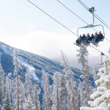 Group of people riding chair lift up a mountain with skis on Kindred Resort Keystone