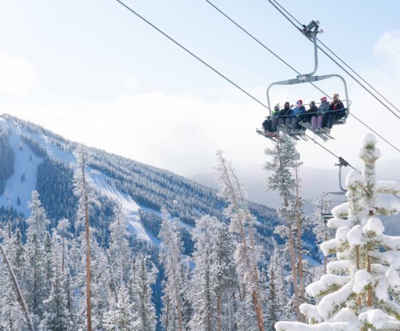 Group of people riding chair lift up a mountain with skis on Kindred Resort Keystone