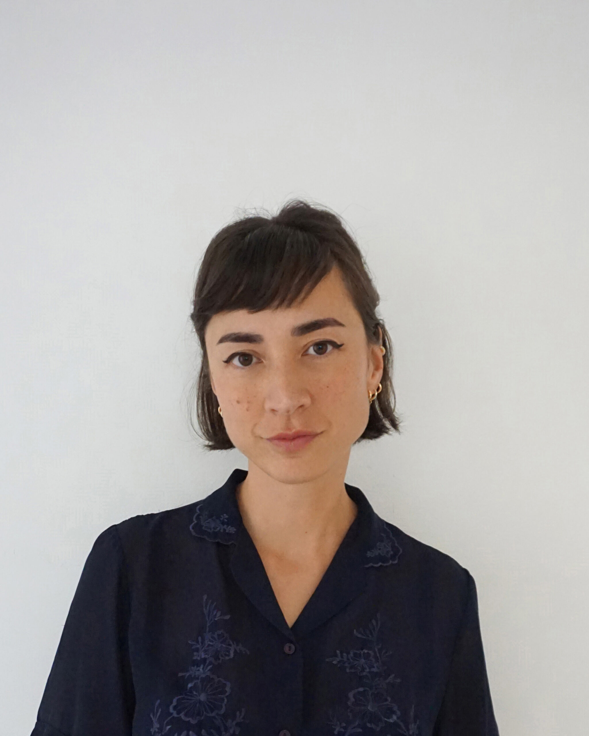 Woman with short dark hair posing against plain white wall