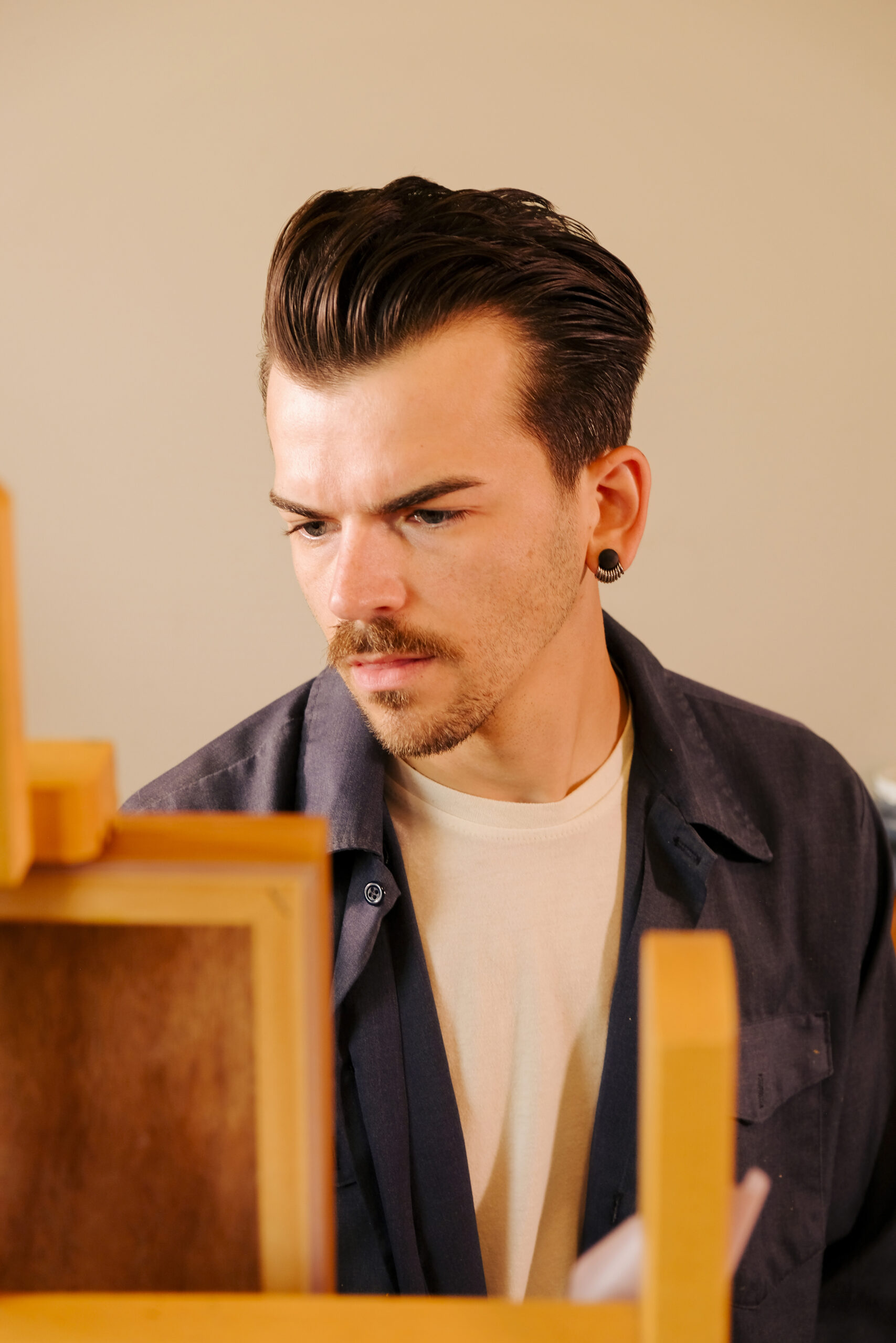 Man with slicked-back hair and mustache looking at artwork in a studio