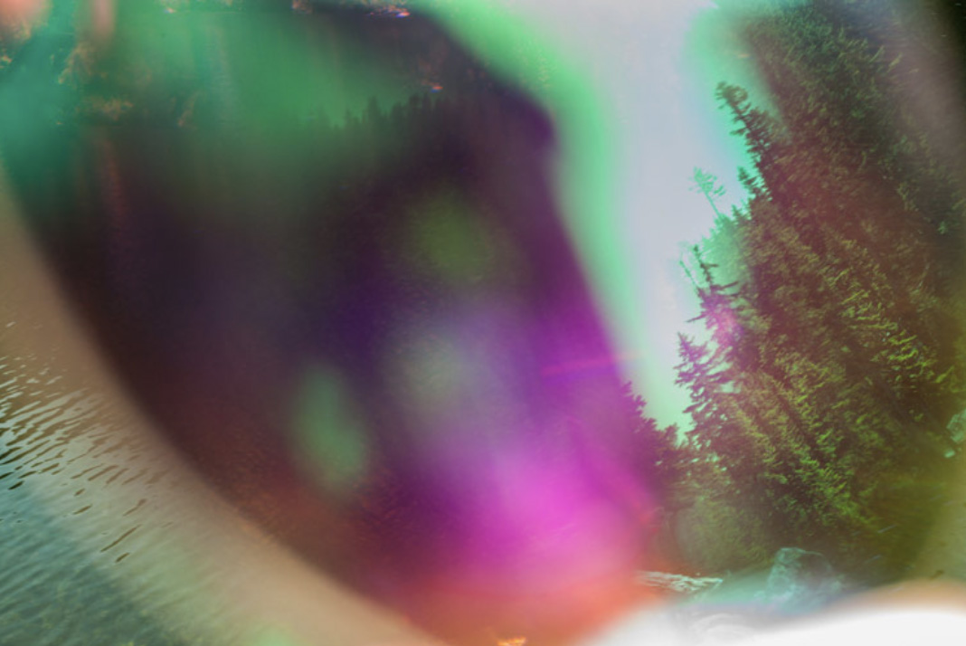 Forest and water scene obscured by prismatic blur and saturated color streaks