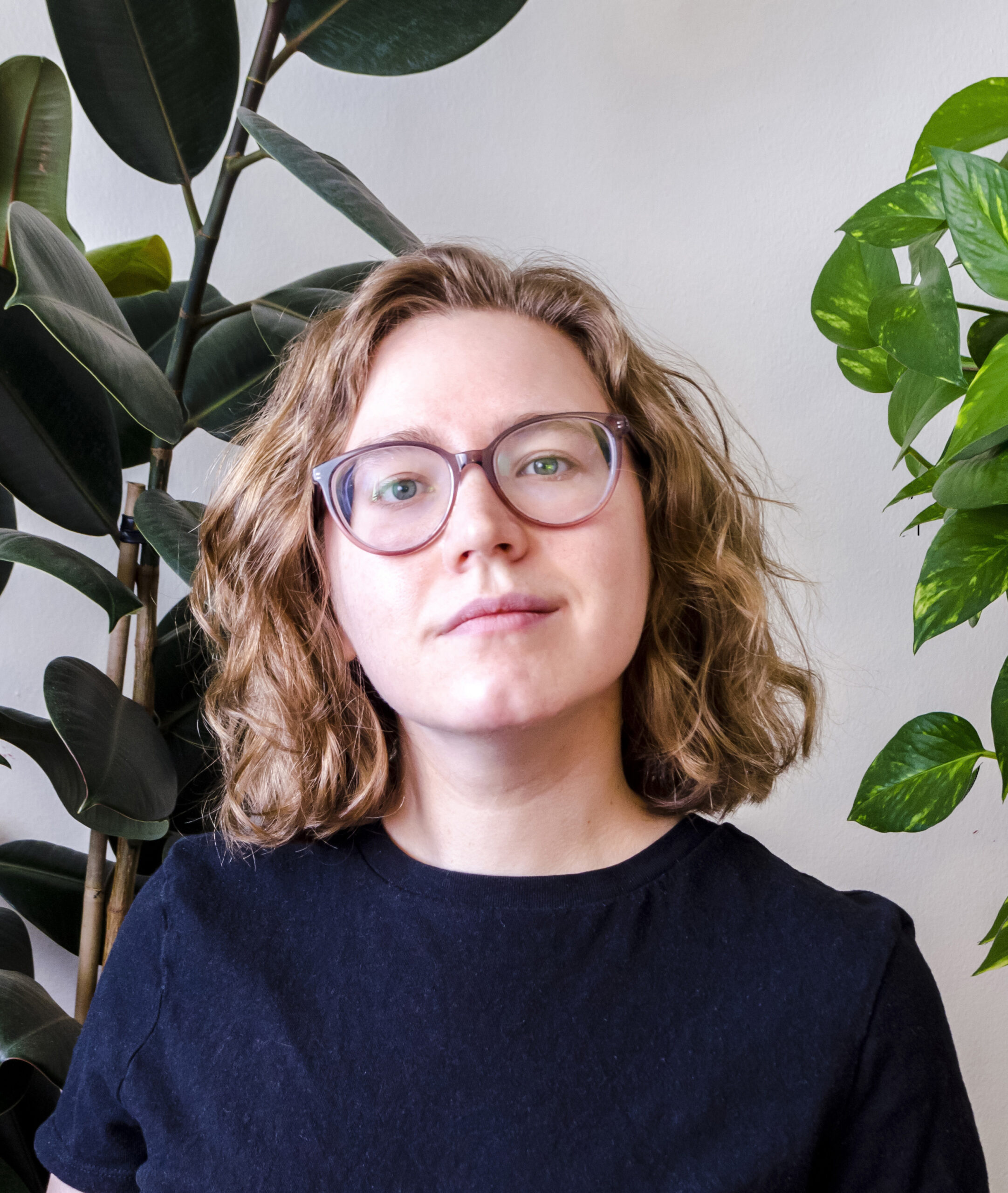 Woman with glasses in black shirt standing between indoor plants
