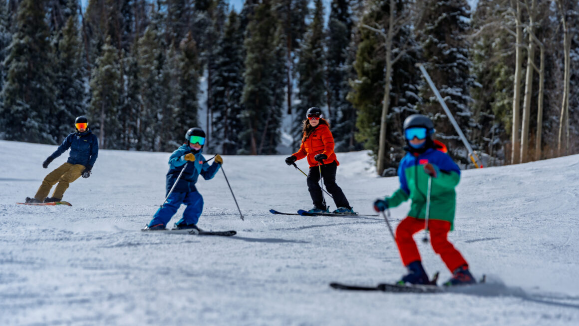 Four people skiing and snowboarding on snowy mountain slope.